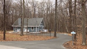 A house with a grey roof and white trim, surrounded by leaf-covered ground and trees.