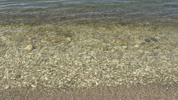 A clear view of a pebble beach with calm water and a distant shoreline.