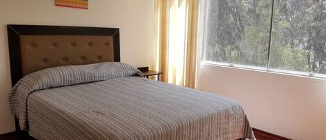 A single bed with a striped bedspread and a tufted headboard in a room with a window and curtains.