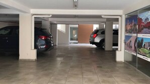 Un parking couvert où sont garées deux voitures, avec un sol carrelé et un mur en verre orné de tableaux.