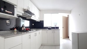 Une cuisine moderne avec des meubles blancs, une hotte en acier inoxydable, une cuisinière à gaz et un four à micro-ondes.