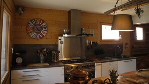 Uma cozinha com paredes de madeira, um relógio grande, um fogão e um lustre.