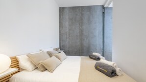 A modern hotel room with a large bed, multiple pillows, a bedside table, and a towel rack. - Penthouse Dalias with private jacuzzi in Port de Pollensa (Puerto Pollensa)