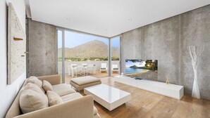 A modern living room with a large TV, beige sofas, a white coffee table, and a view of a mountainous landscape through large windows. - Penthouse Dalias with private jacuzzi in Port de Pollensa (Puerto Pollensa)