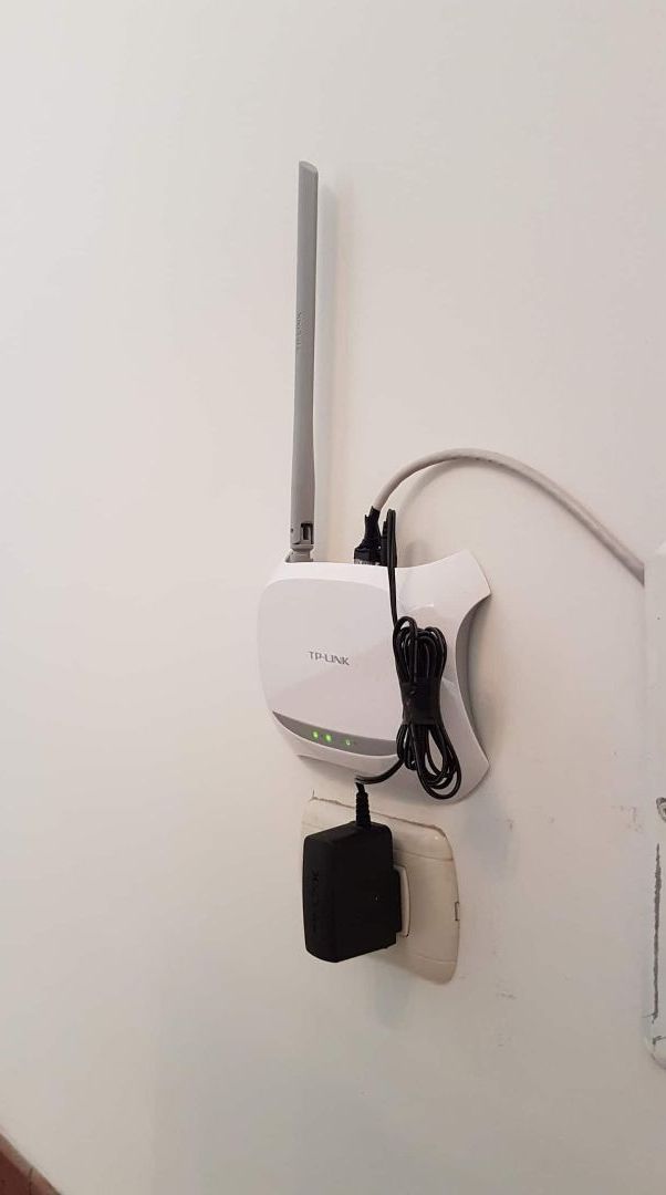 A TP-Link router mounted on a white wall with a power adapter plugged in.