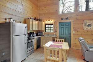 Cozy cabin-style kitchen with a dining table and leather chair, featuring a stainless steel refrigerator, oven, and wooden cabinets.