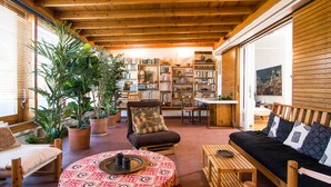 Una sala de estar acogedora con techo de madera, un sofá, una silla, una mesa de centro y una estantería llena de libros.