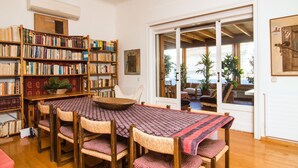 Un acogedor salón de lectura con una mesa de madera, sillas y una estantería llena de libros.