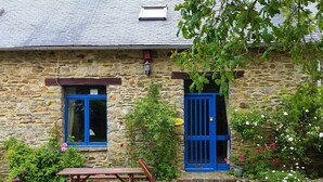 A stone building with a blue door and window, a wooden bench, and a gravel path.
