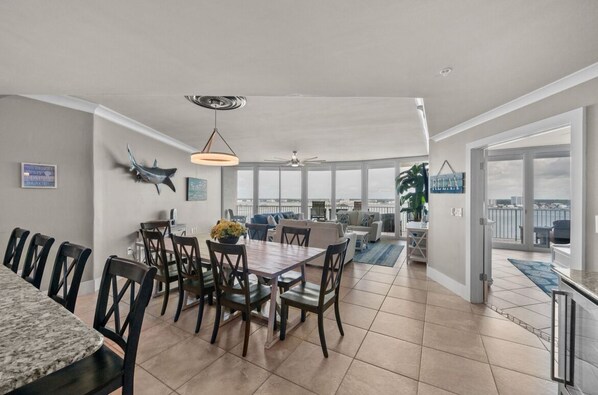 A spacious living area with a dining table, chairs, and a view of the city through large windows. - DOWN BY THE BAY! ASK ABOUT DISCOUNTS! 3 Bedroom Unit Amazing bay views! (Orange Beach)