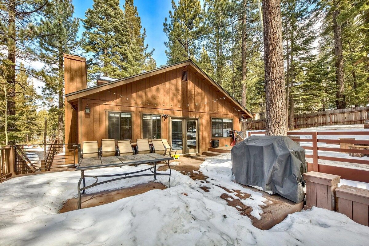 A wooden cabin with a patio, surrounded by trees.
