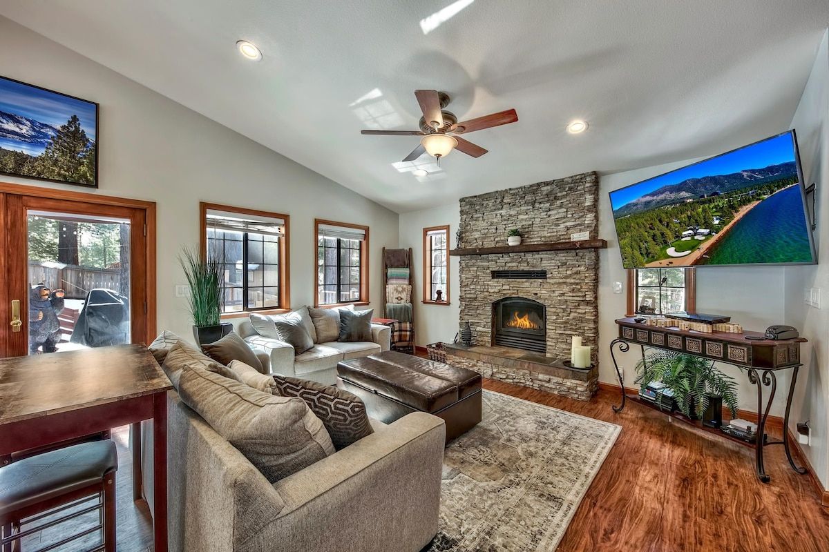 A spacious living room with a stone fireplace, a large flat-screen TV, and a ceiling fan.