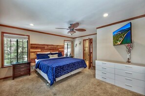 Un dormitorio con cama, cómoda, ventilador de techo y televisor que muestra un paisaje pintoresco.