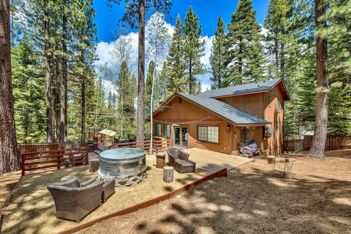 Eine Hütte mit Terrasse, Whirlpool und Sitzbereich im Freien, umgeben von hohen Bäumen.