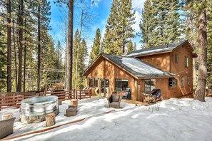 A wooden cabin with a deck, surrounded by snow and tall trees.