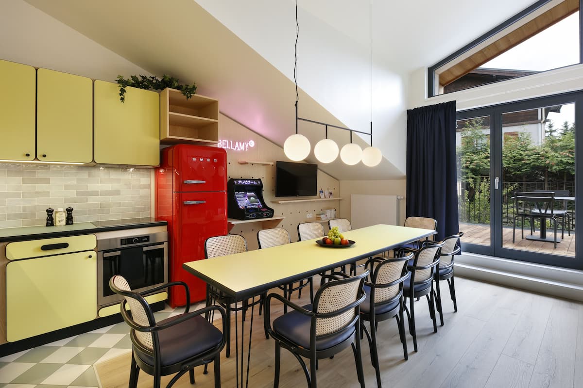 A modern kitchen with yellow cabinets, a red refrigerator, and a dining area with a long table and chairs.