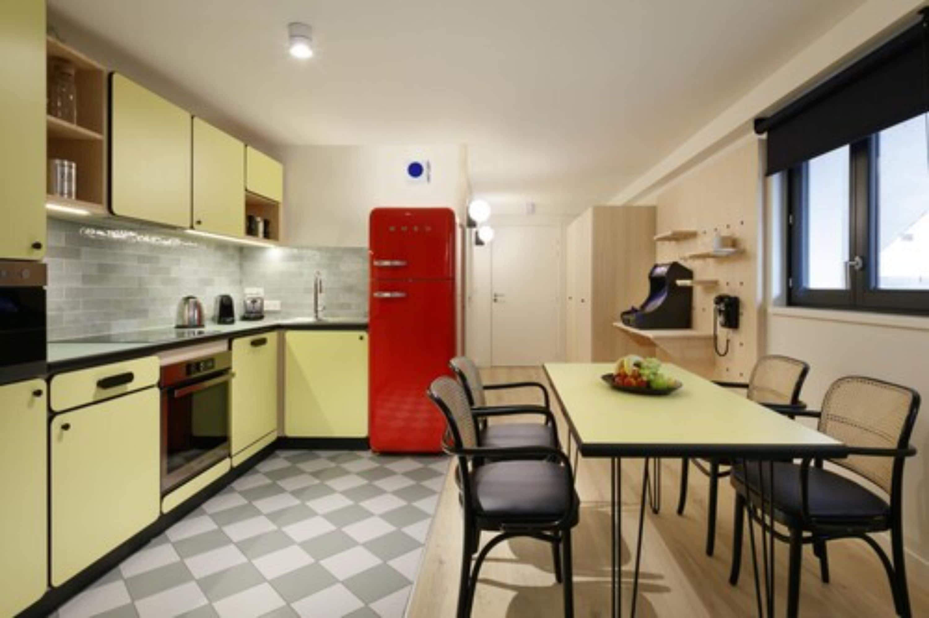 A compact kitchen with yellow cabinets, a red refrigerator, and a dining area with four chairs.