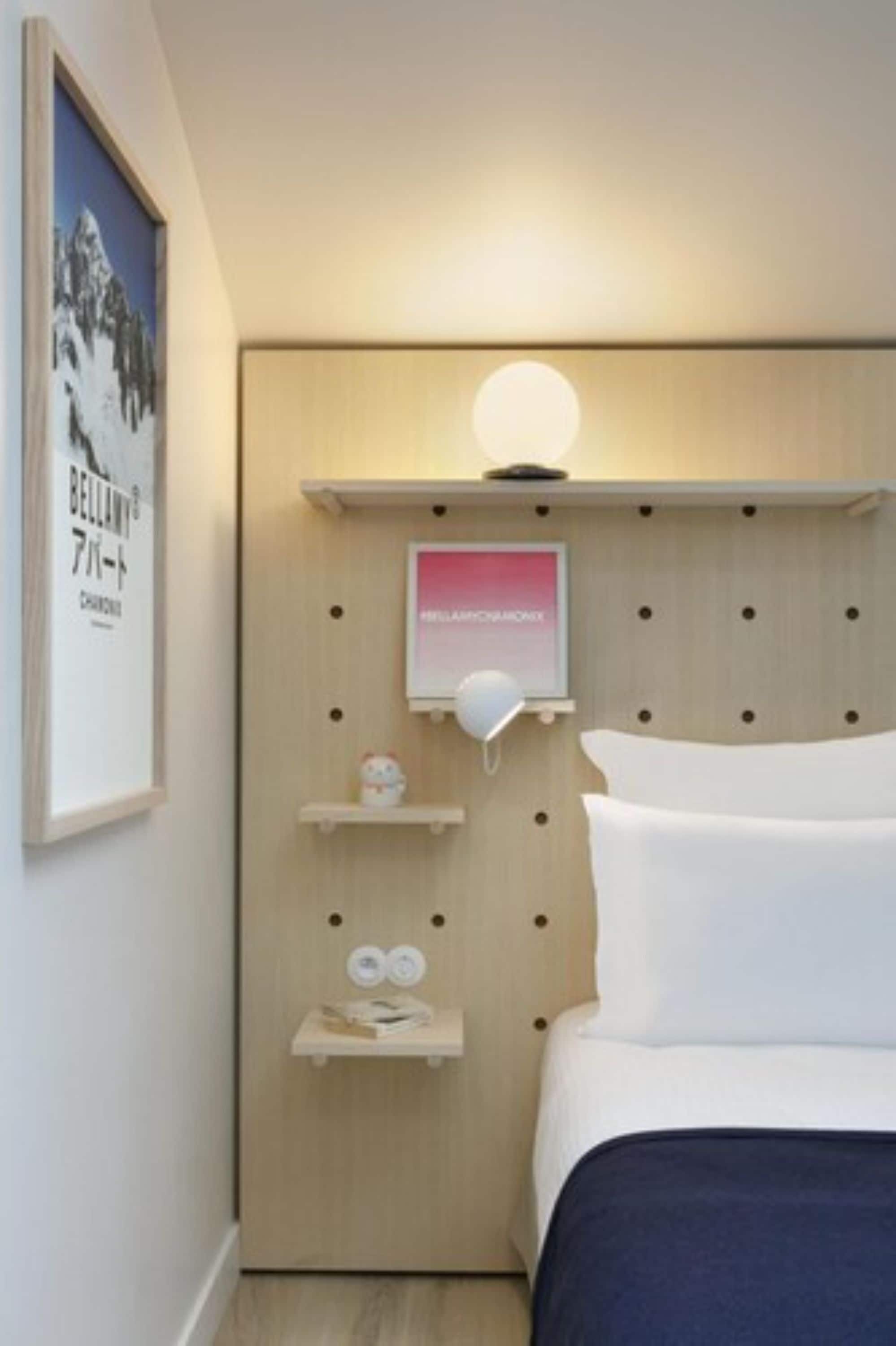 Een hotelkamer met een houten hoofdbord, een bedlamp, een lijst met een afbeelding en een klein plankje met een decoratief object.