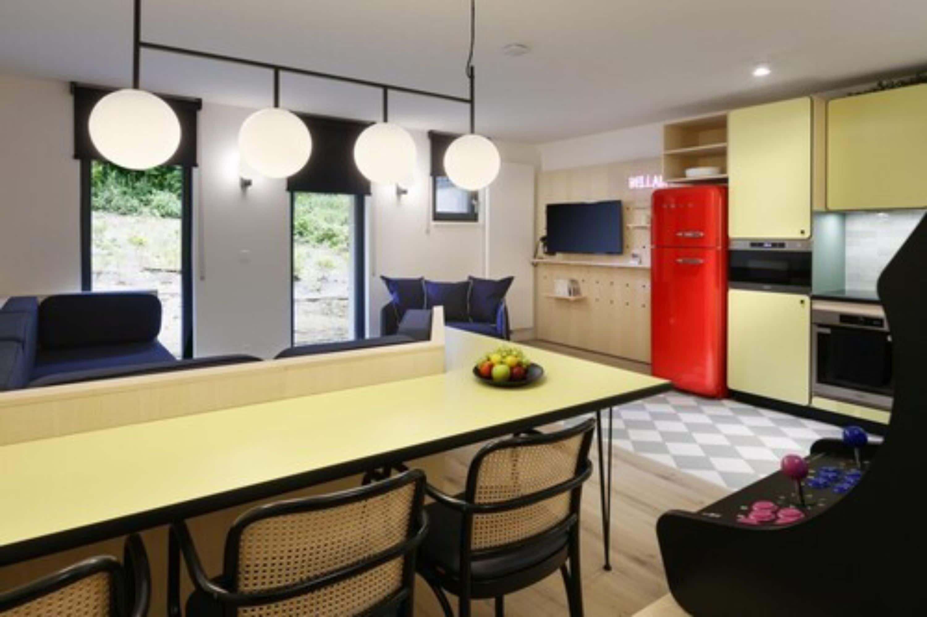 Una cocina moderna con una isla central, una zona de comedor con sillas y un refrigerador rojo.