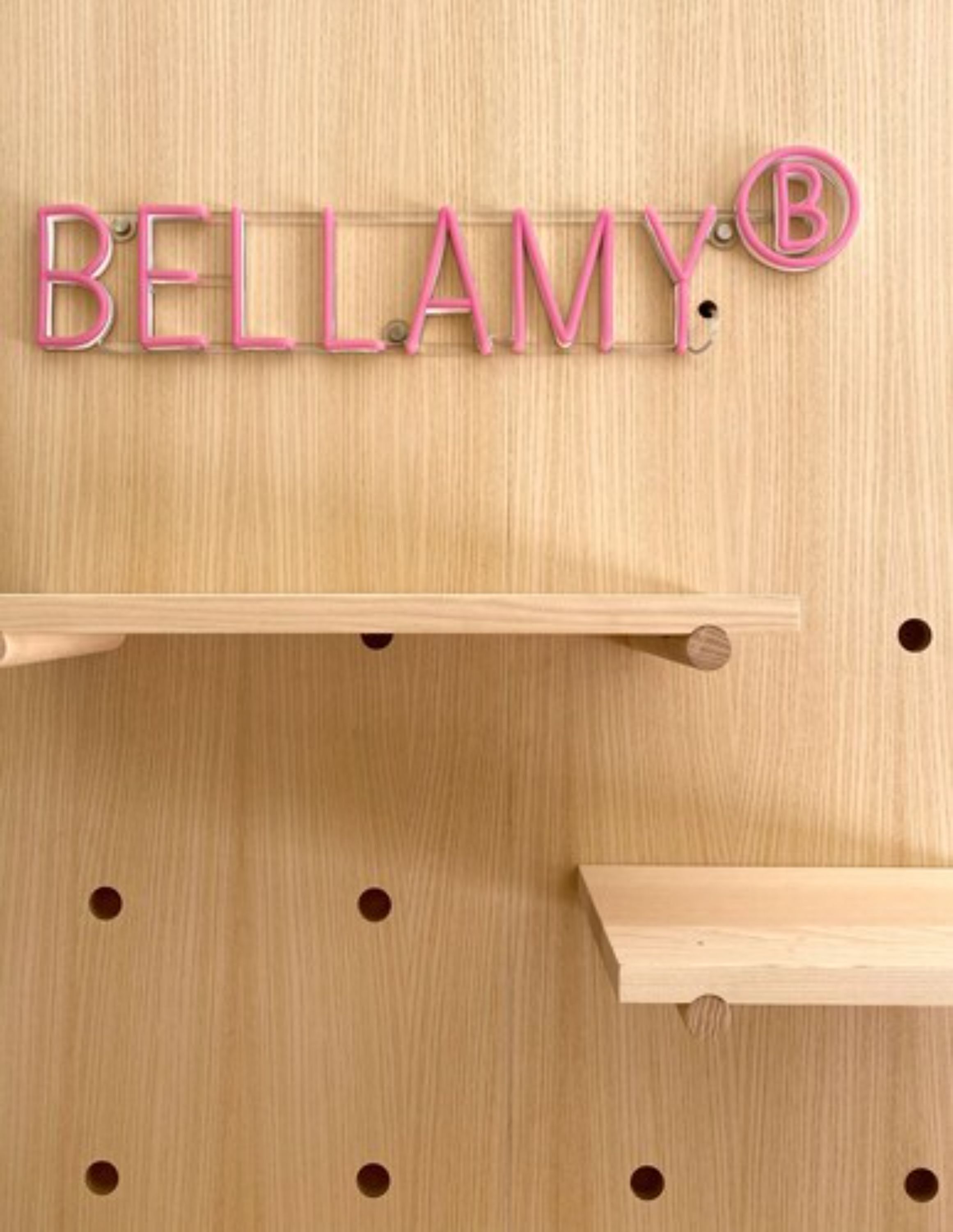 Een houten wand met de naam 'BELLAMY' in roze letters en een geregistreerd handelsmerk.