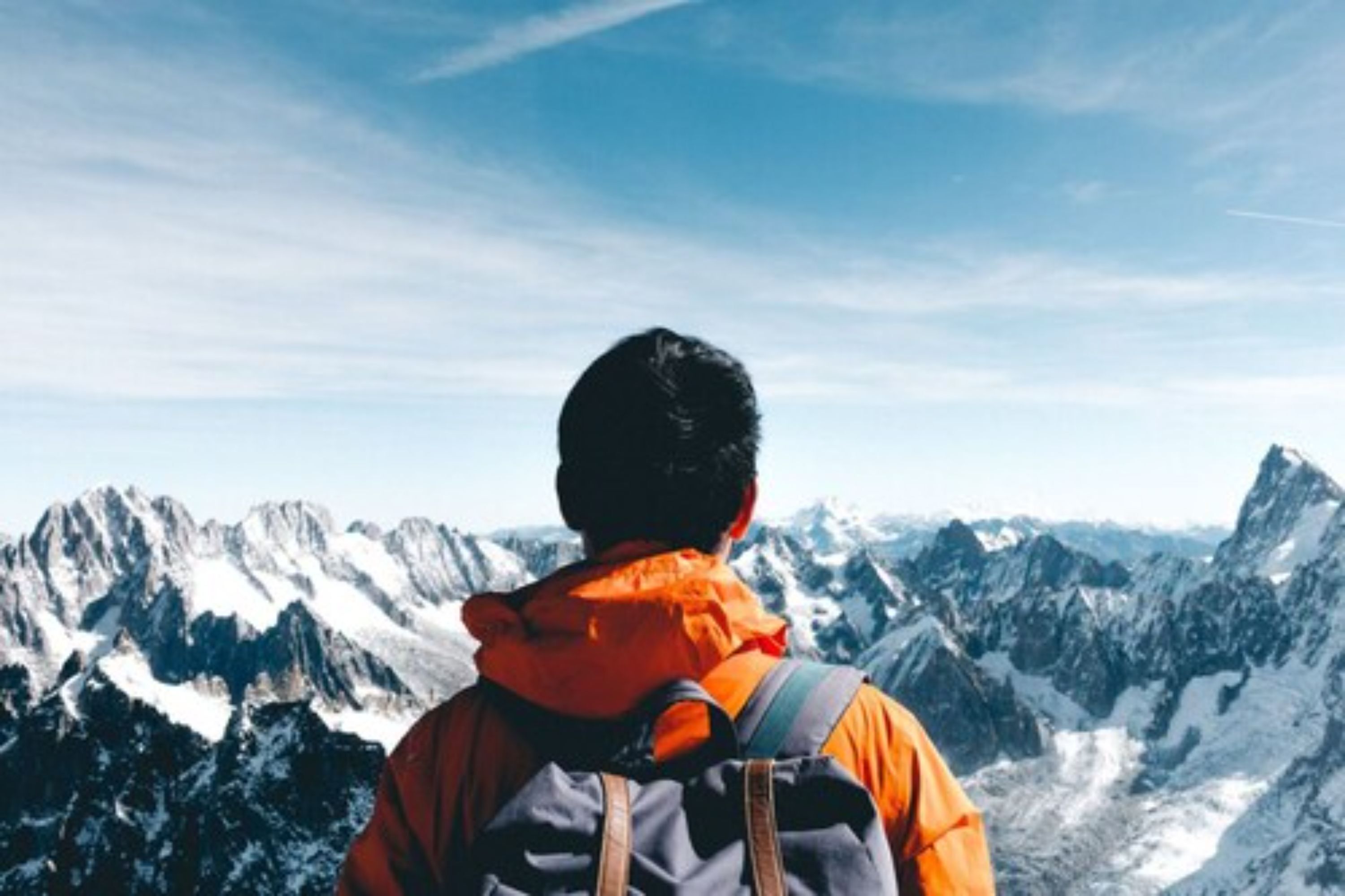 A person in an orange jacket with a backpack, overlooking a mountainous landscape.