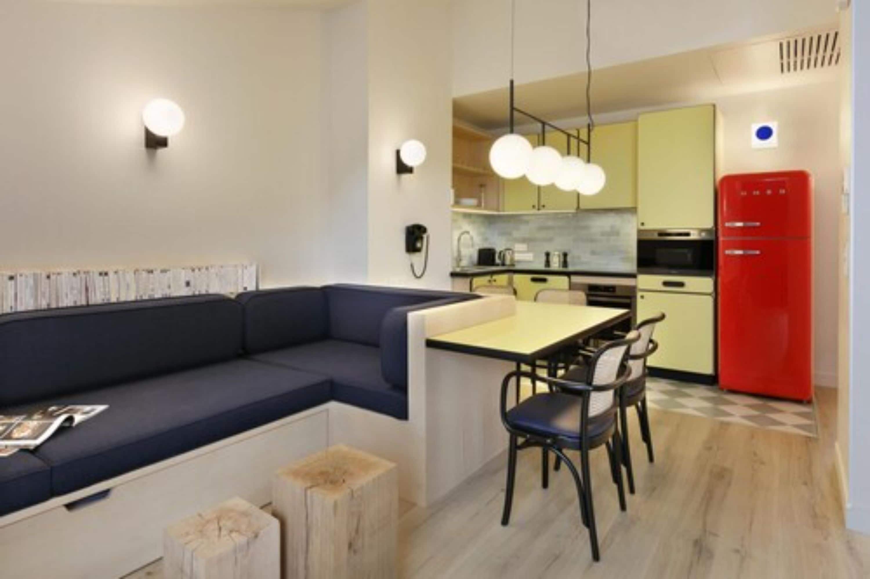 A compact kitchen with a dining area, a red refrigerator, and a blue sofa.