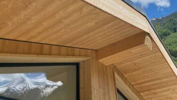 A modern wooden cabin with large windows, a sloped roof, and a view of a mountain.