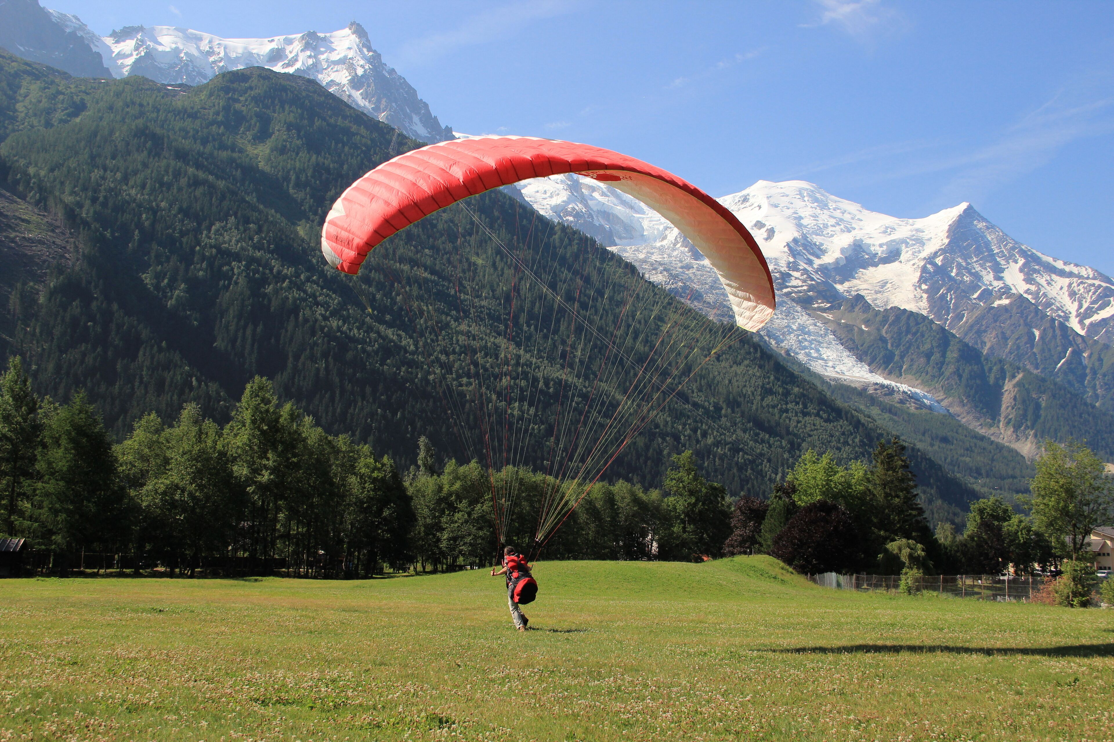 A person paragliding over a grassy field with a mountainous backdrop.