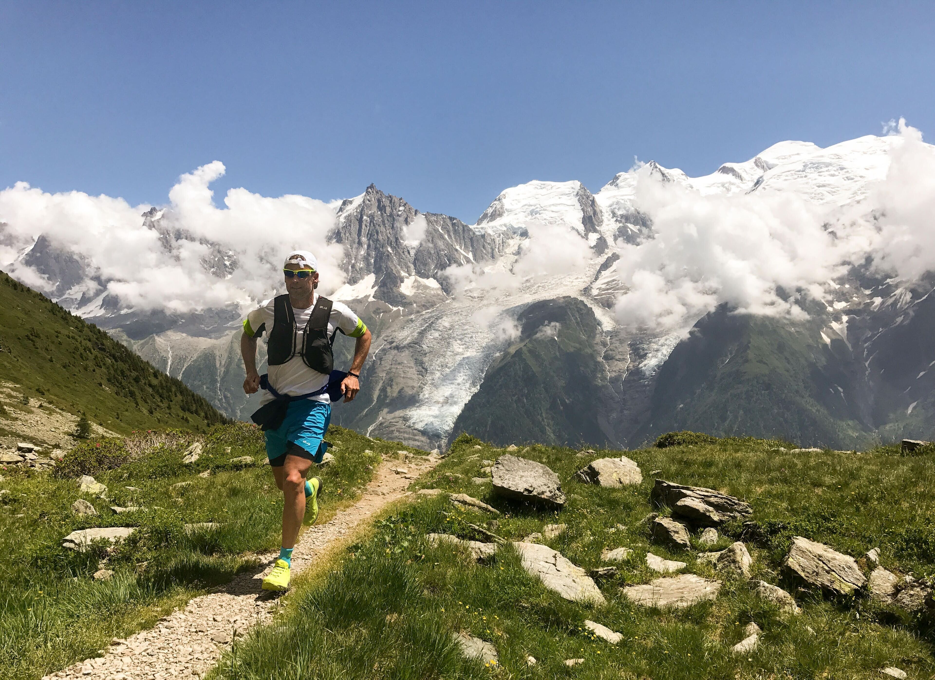 A hiker on a mountain trail with snow-capped peaks in the background.