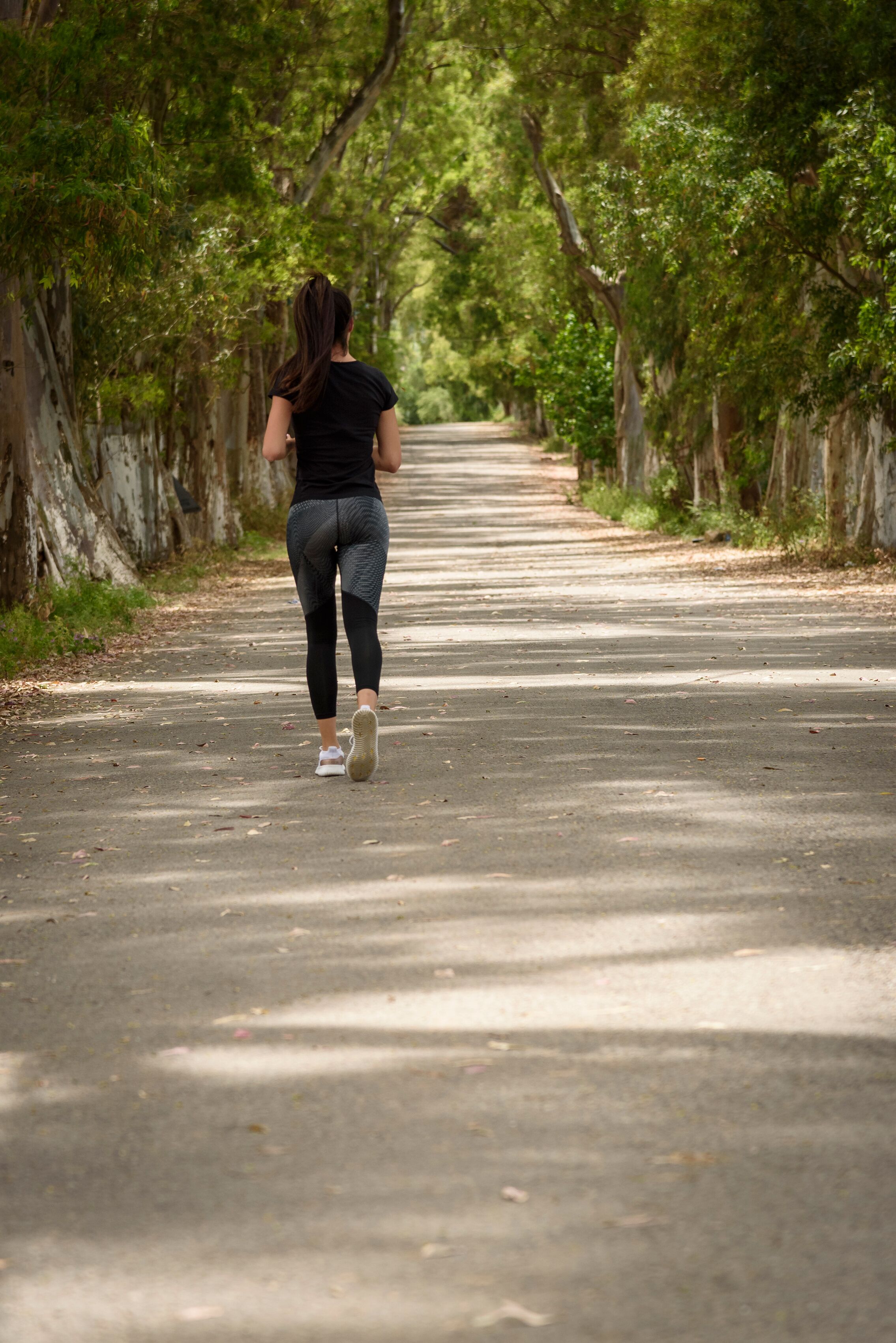 A woman walking down a tree-lined road.