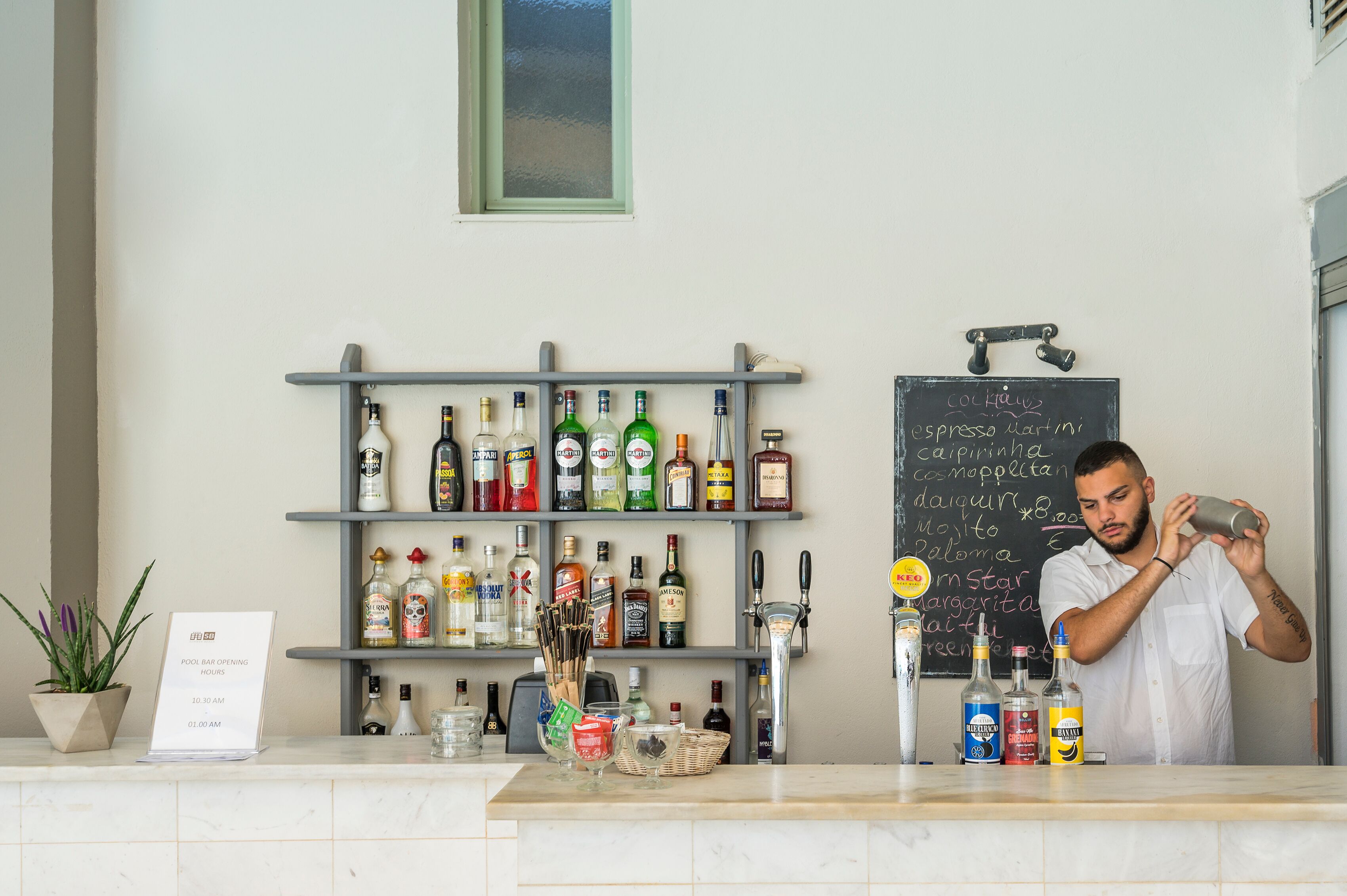 A bar area with shelves of liquor bottles, a chalkboard menu, and a bartender preparing a drink.