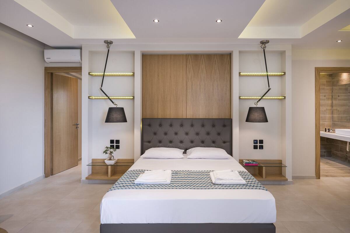 Een moderne hotelkamer met een groot bed, twee nachtkastjes, een wandairconditioner en een badkamer aan de rechterkant.