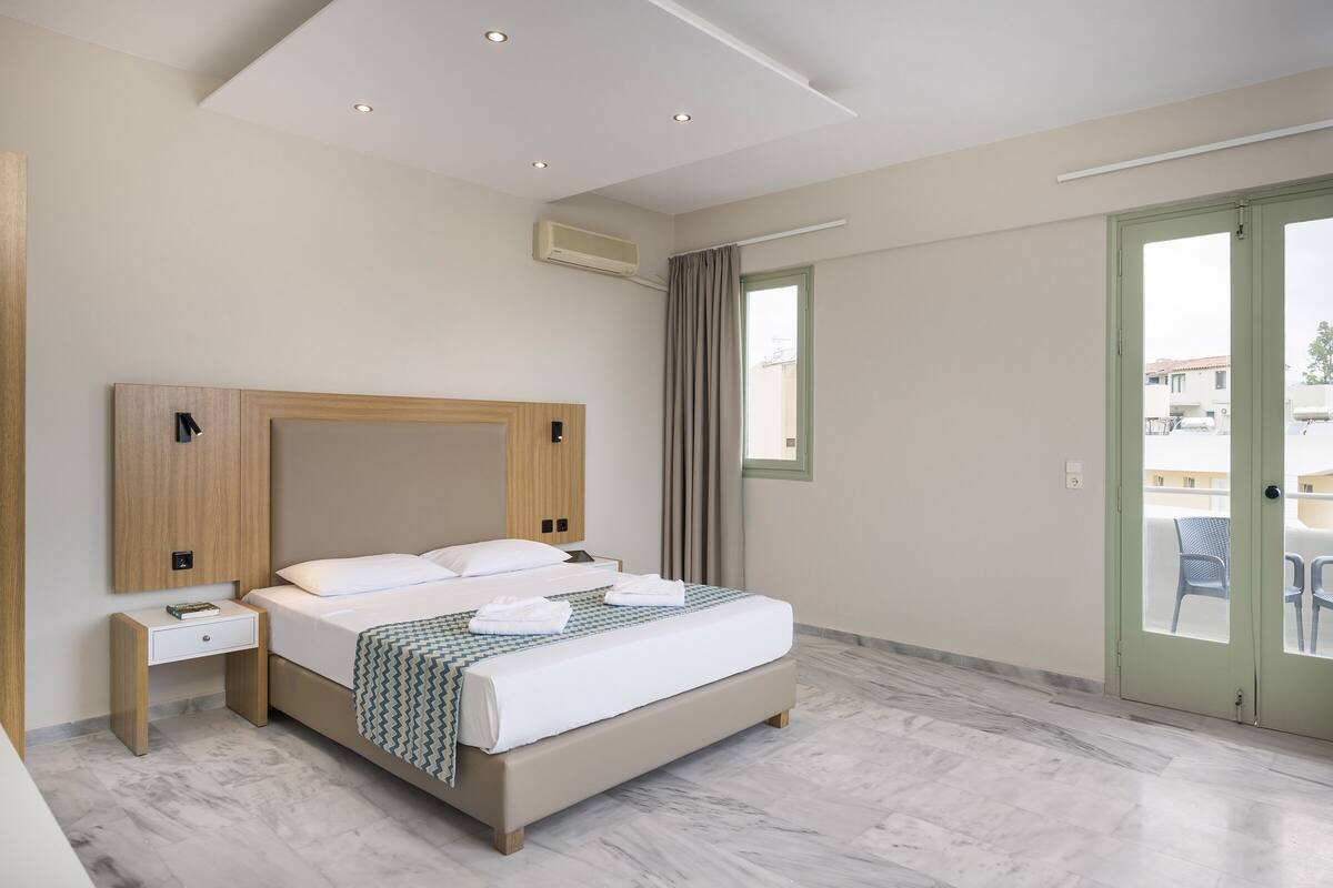 Een moderne hotelkamer met een groot bed, een nachtkastje, een raam met gordijnen en een uitzicht op het buitenbalkon.