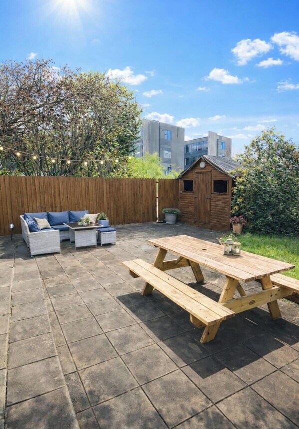 A patio area with a wooden table and benches, a sofa set, and a small wooden shed. - Shangri La Spacious Town House free carpark (Killarney)