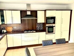 A kitchen with a gas stove, microwave, oven, and a dining area with two chairs. - Shangri La Spacious Town House free carpark (Killarney)