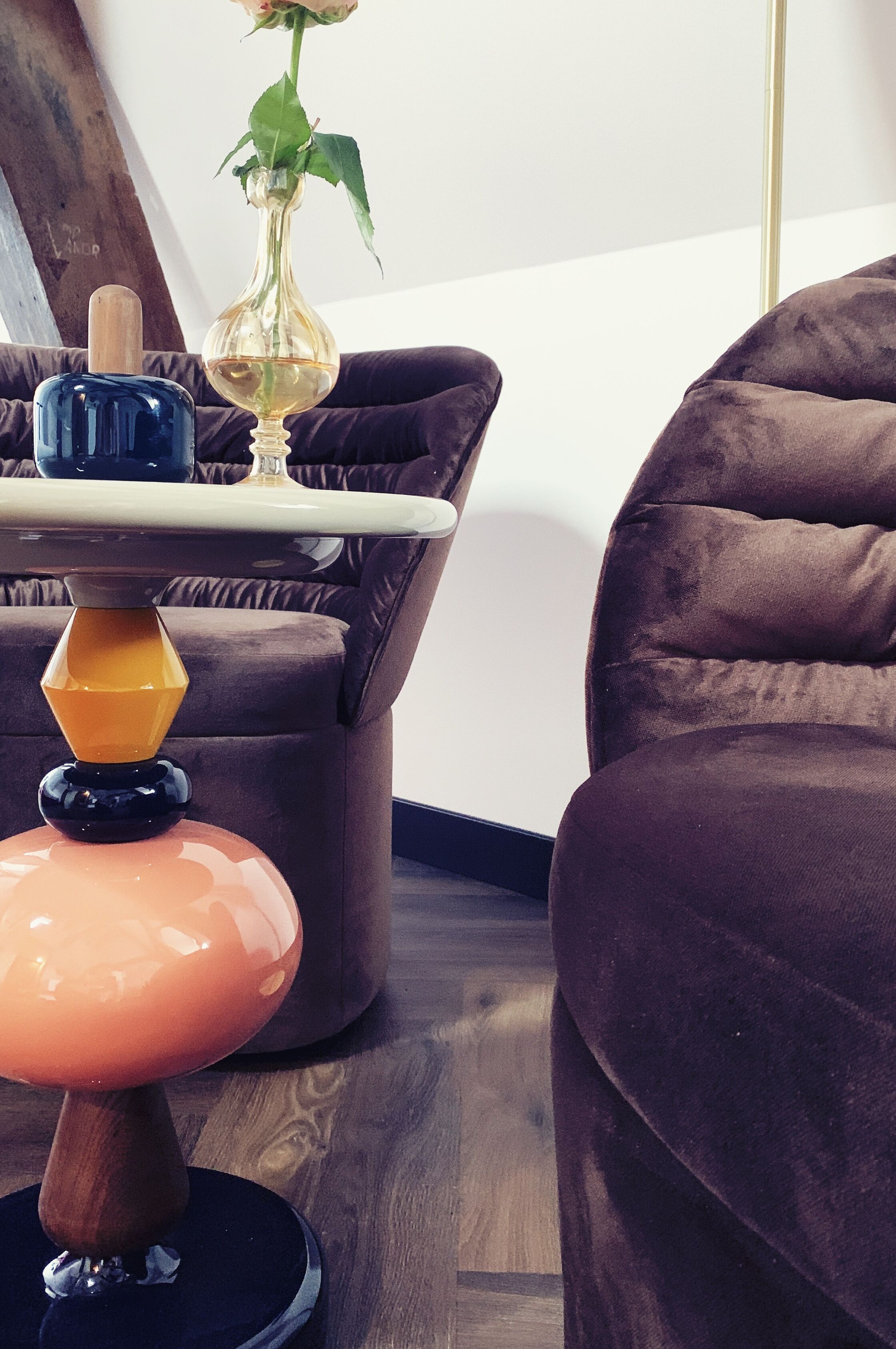 Una sala moderna con un sofá marrón oscuro, una mesita redonda con un jarrón de flores y una lámpara única naranja y negra.
