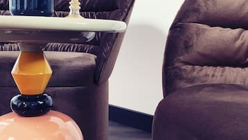 Una sala moderna con un sofá marrón oscuro, una mesita redonda con un jarrón de flores y una lámpara única naranja y negra.