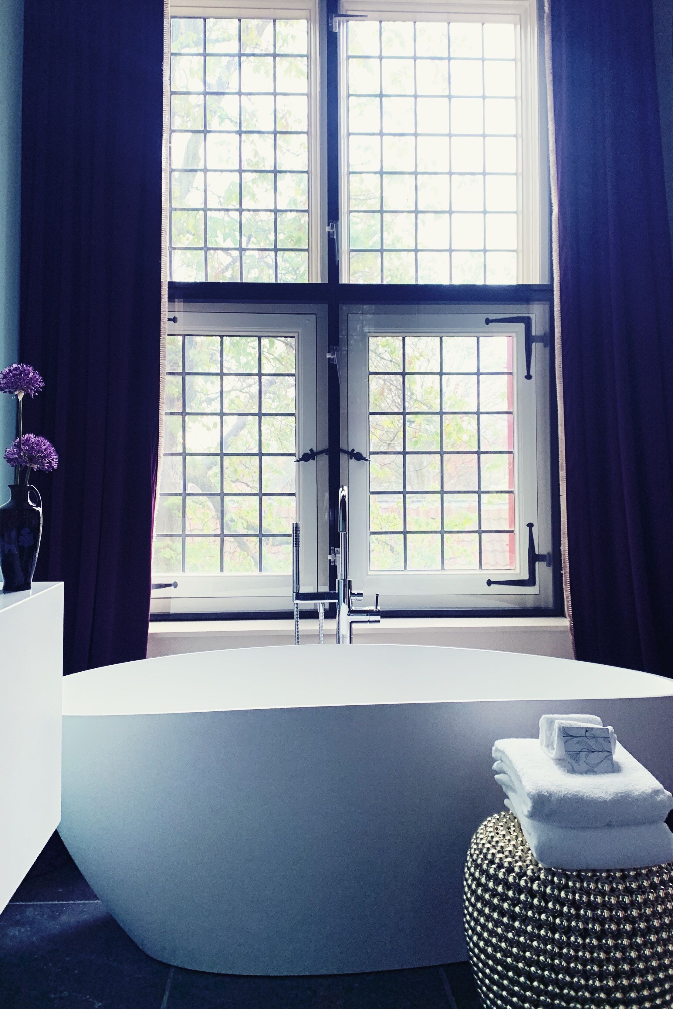 Un baño moderno con una bañera independiente, un tocador con un florero y una ventana con cortinas.