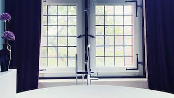 A modern bathroom with a freestanding bathtub, a vanity with a vase of flowers, and a window with curtains.