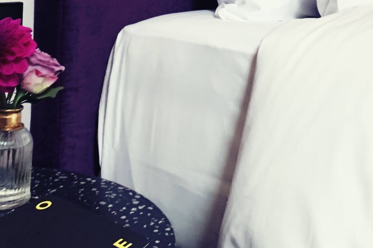 A bed with white linens, a purple headboard, and a gold lamp.