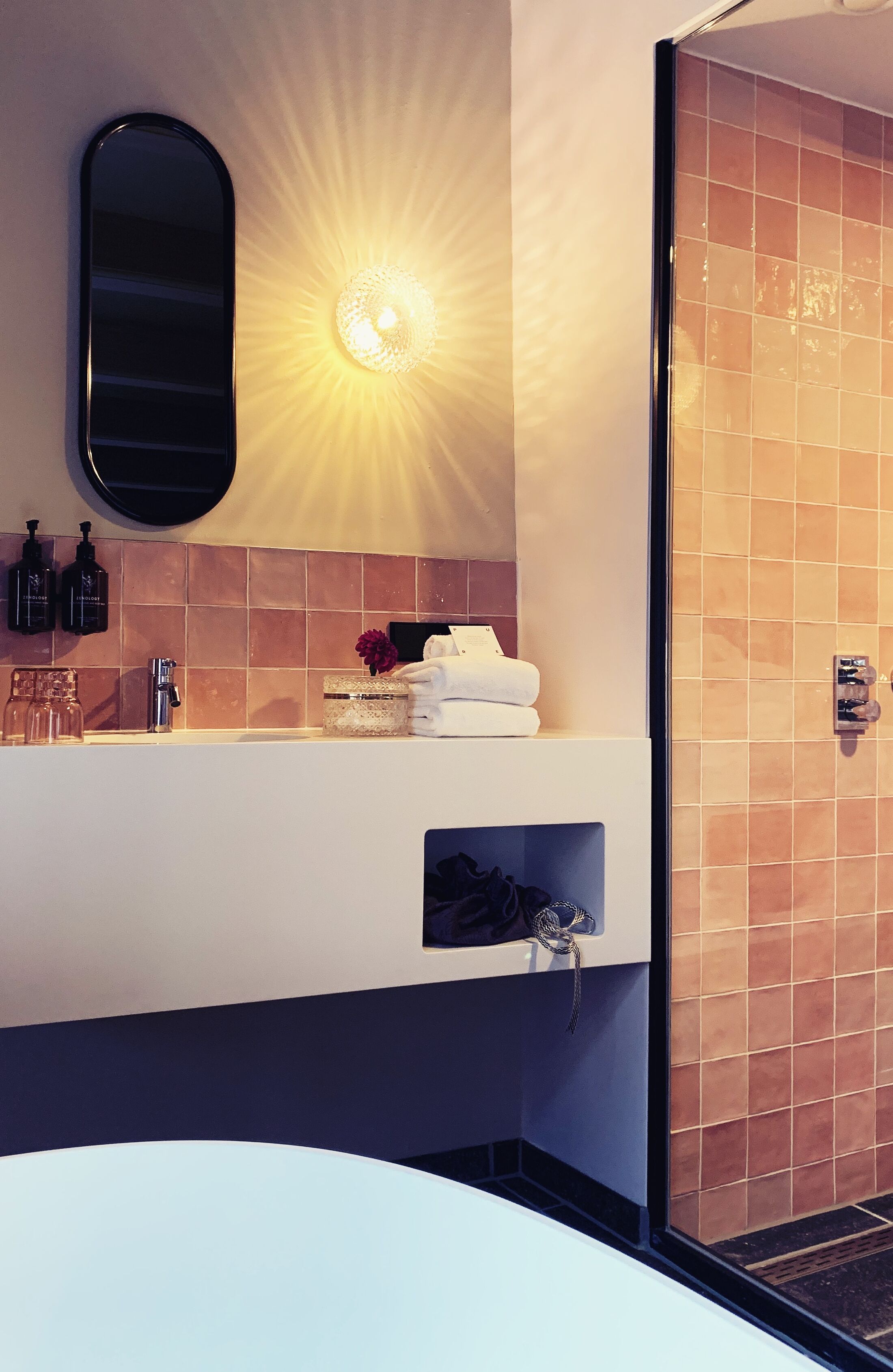 Un baño con espejo, lavabo con artículos de aseo, toallero y zona de ducha.