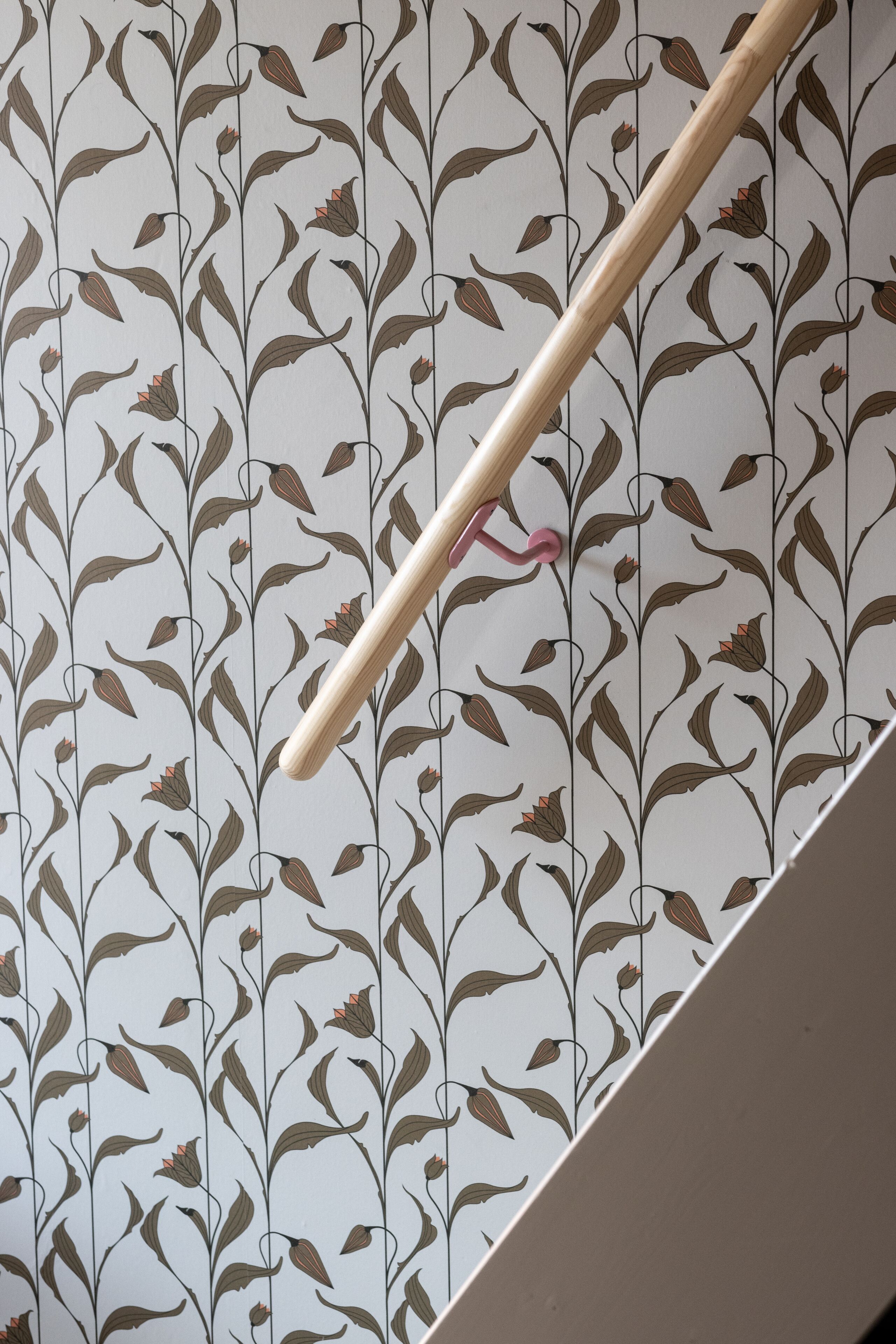 A wooden stick with a pink hook against a wallpaper with a floral pattern.