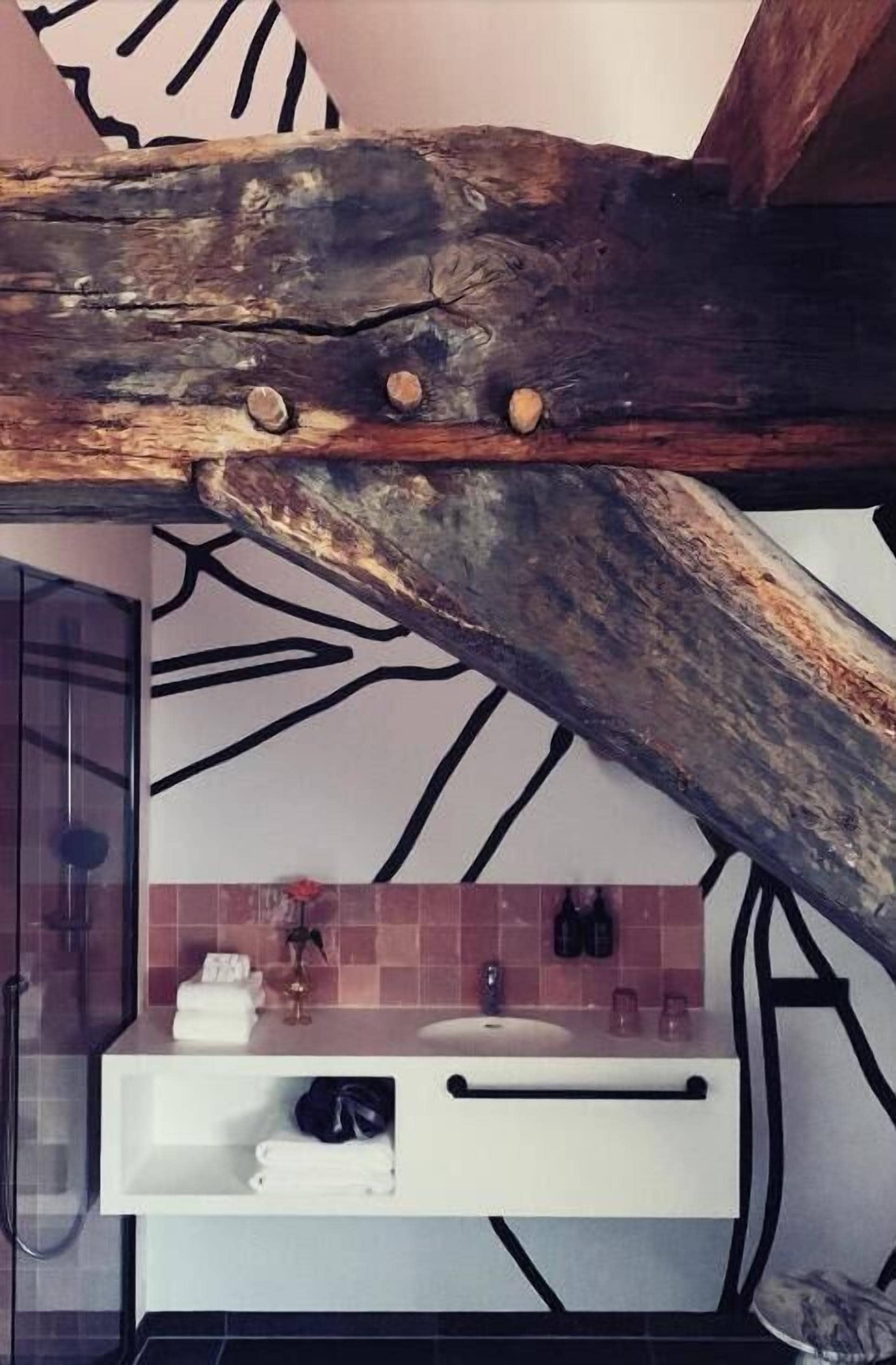 A bathroom with a wooden beam above a sink and a tiled wall with a tree branch design.