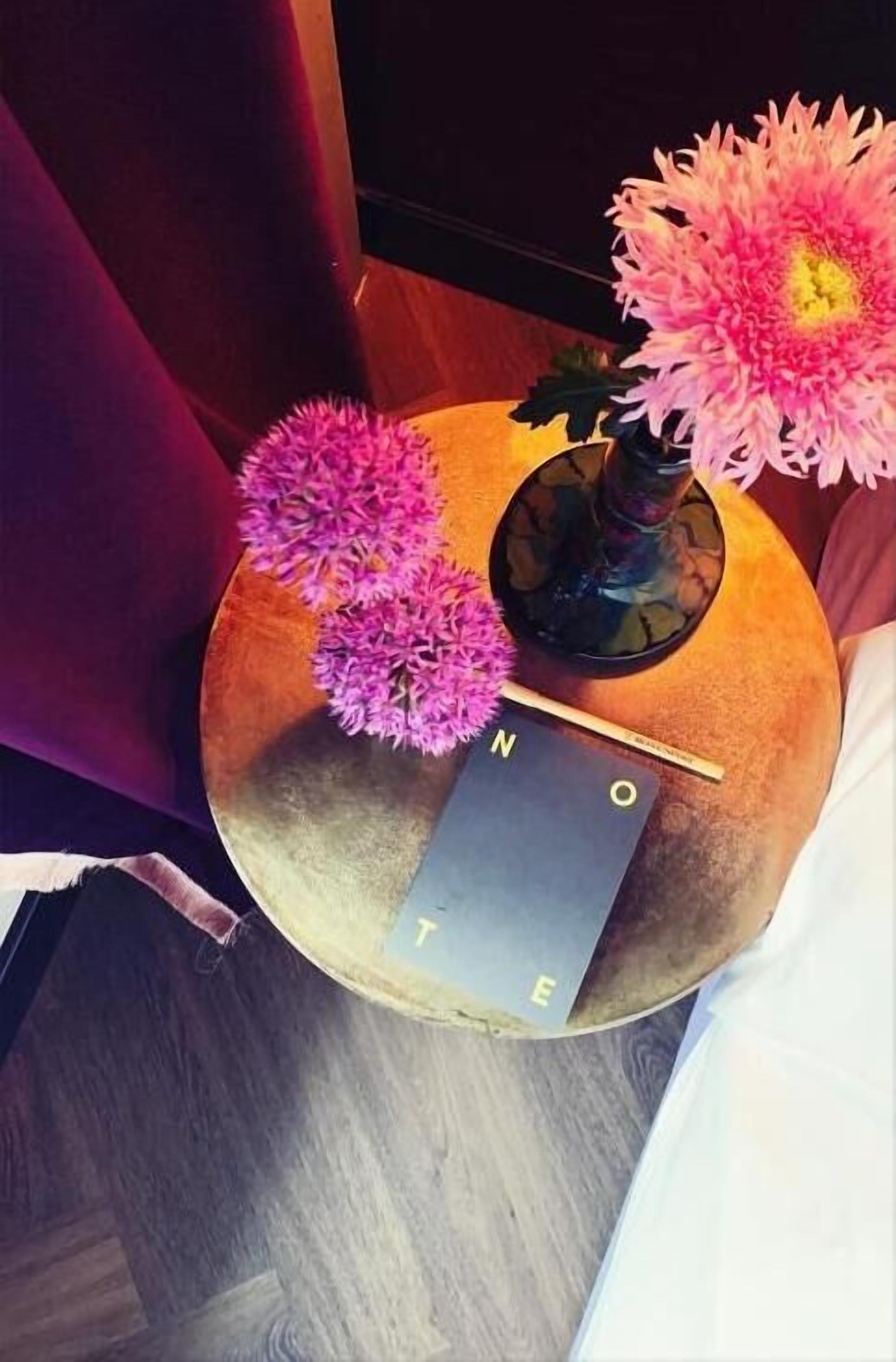 A round table with a vase of pink flowers, a book, and a decorative object.