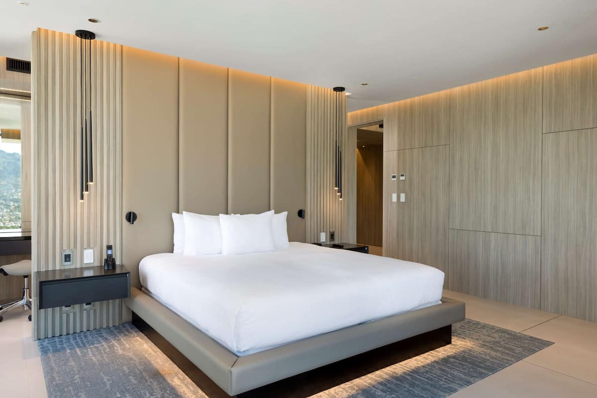 Una habitación de hotel moderna con una cama grande, un escritorio con silla, un armario y un espejo amplio.
