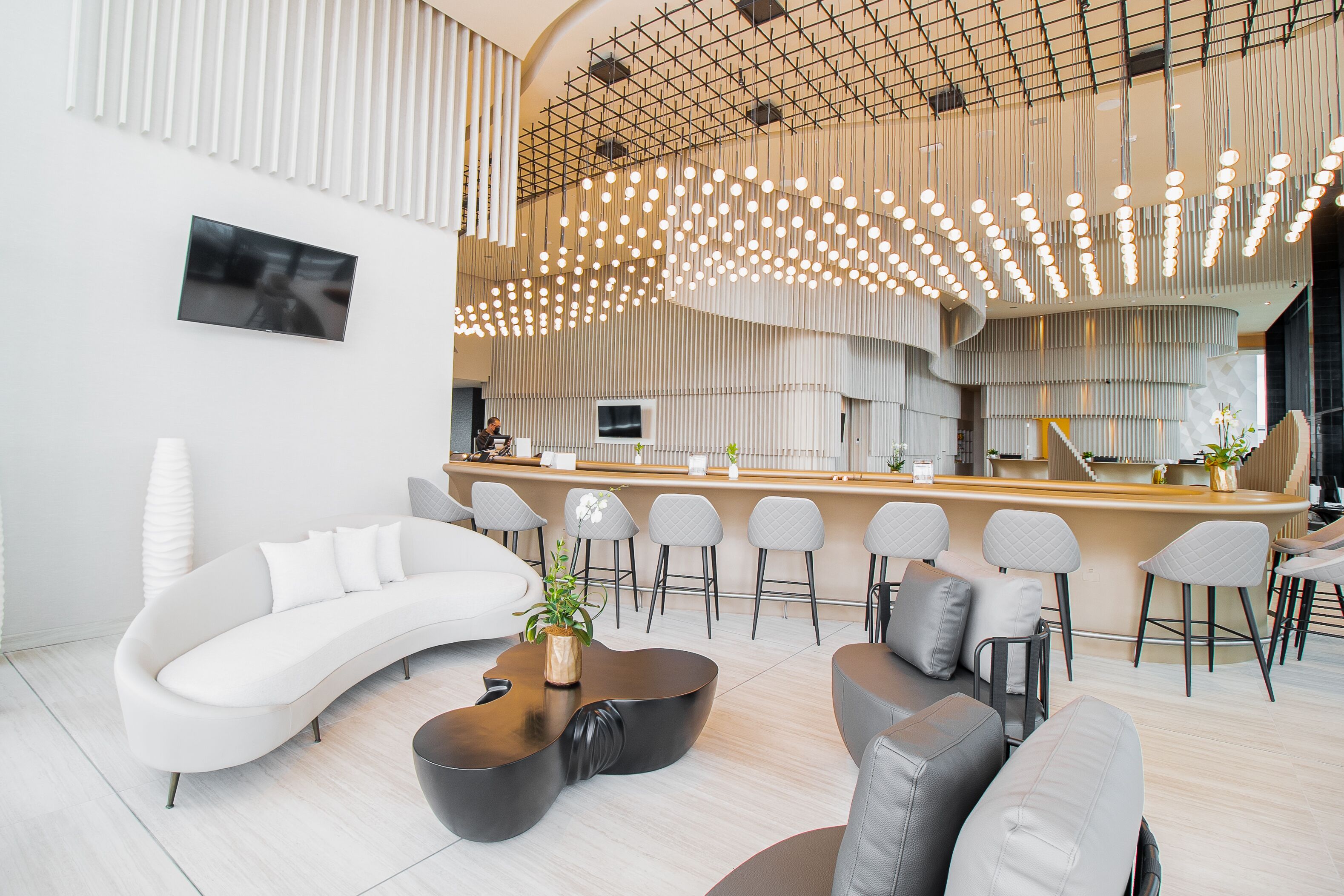 A modern interior with a curved white sofa, a wooden coffee table, and a bar area with stools.