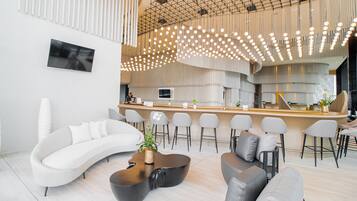 A modern interior with a curved white sofa, a wooden coffee table, and a bar area with stools.