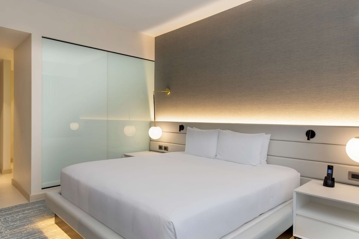 Una habitación de hotel moderna con una cama grande, mesitas de noche, una lámpara de pared y un armario de vidrio.