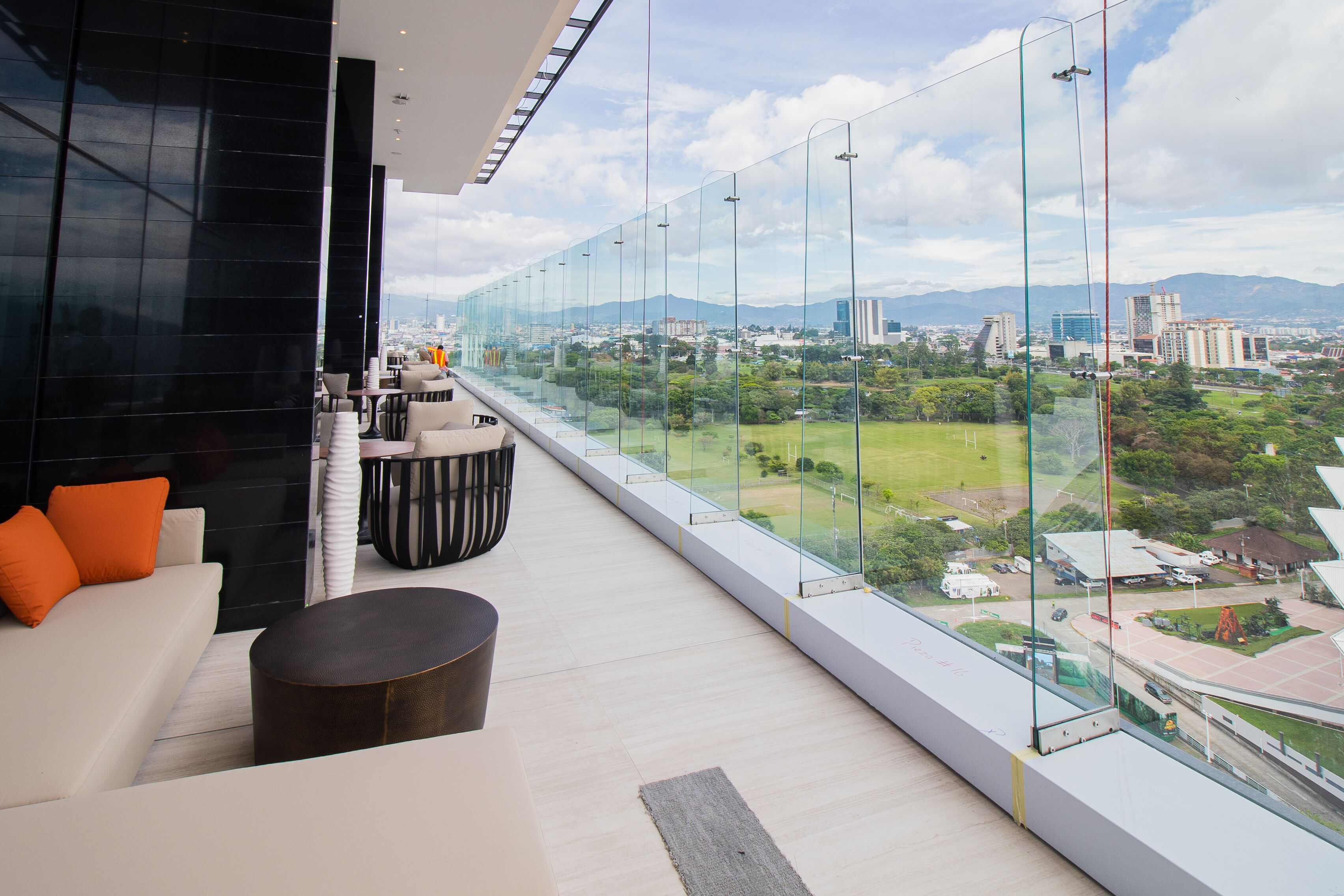 Quarto de hotel moderno com varanda grande, sofá, mesa redonda e vista para a cidade e áreas verdes.