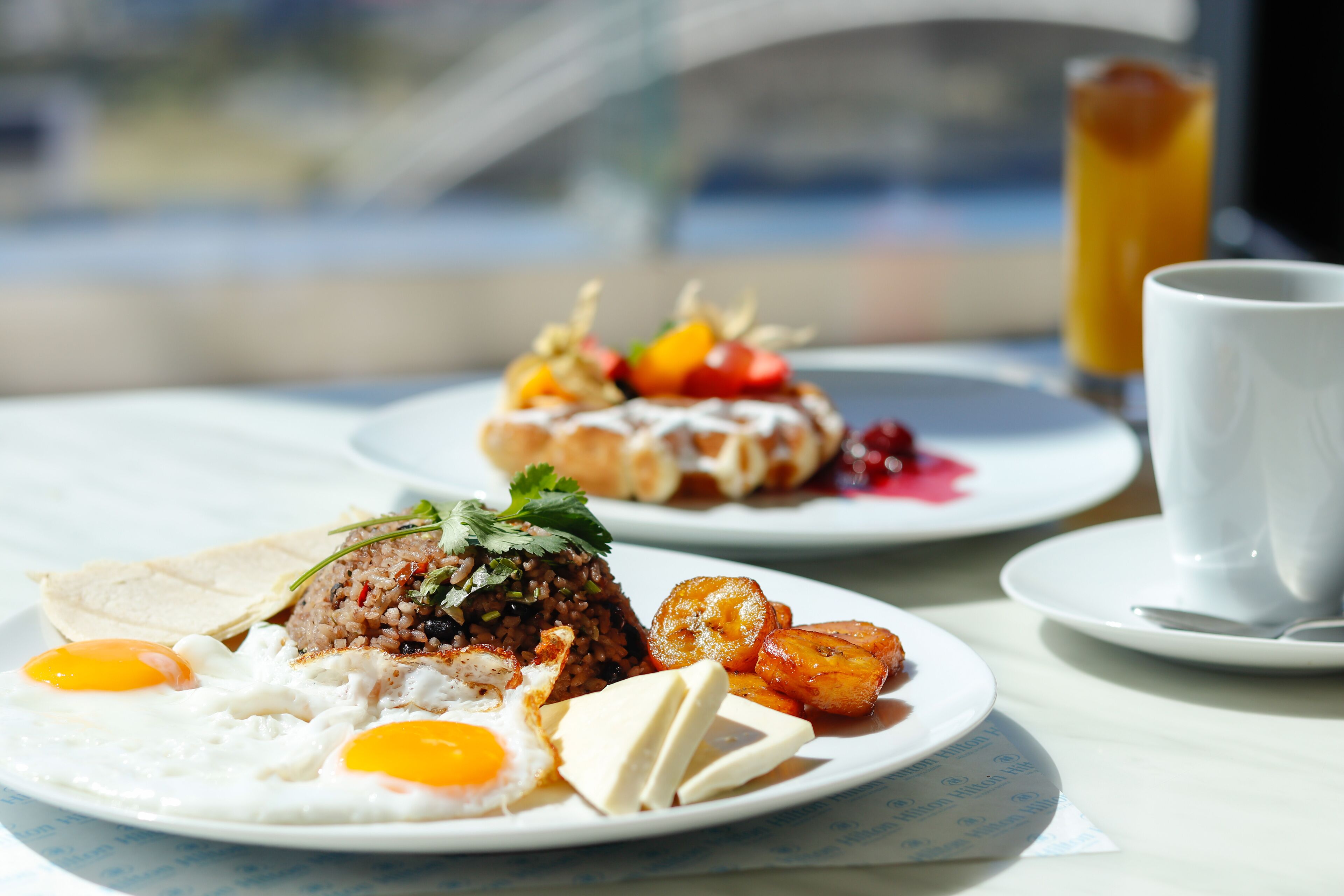 A breakfast setting with plates of food, including eggs, rice, and fruit, and a glass of orange juice.